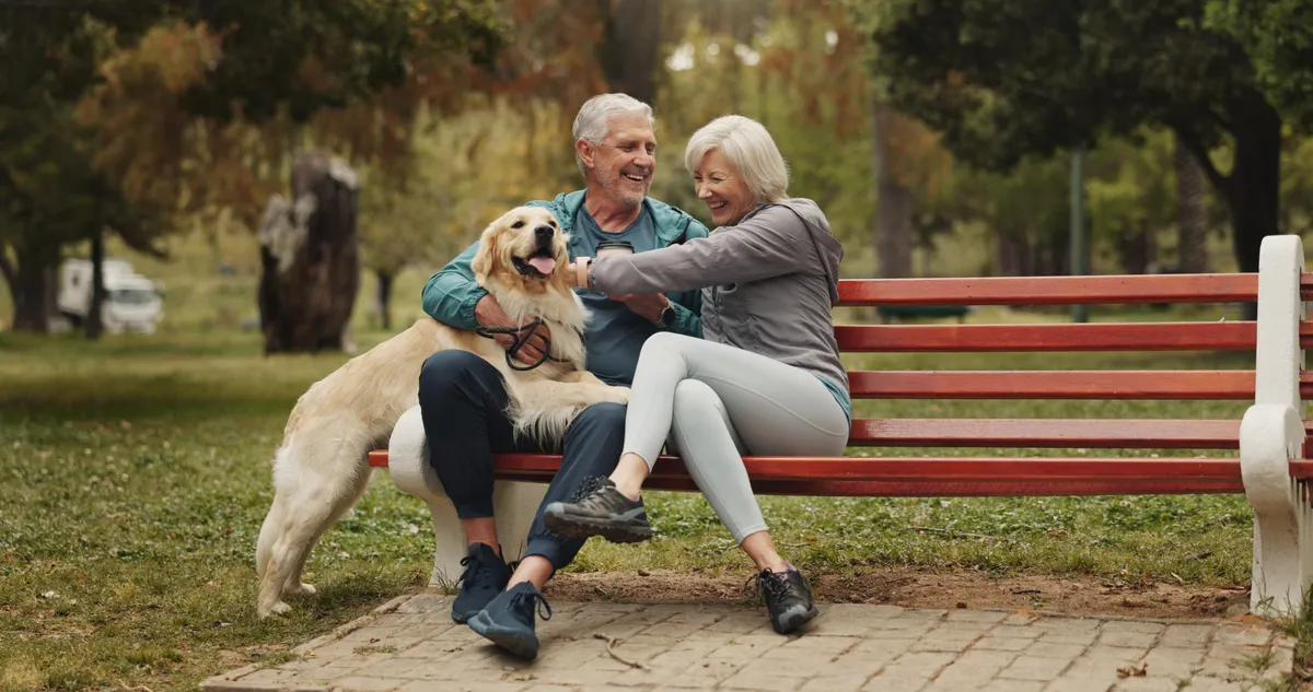 An older couple laughing with their dog on a park bench